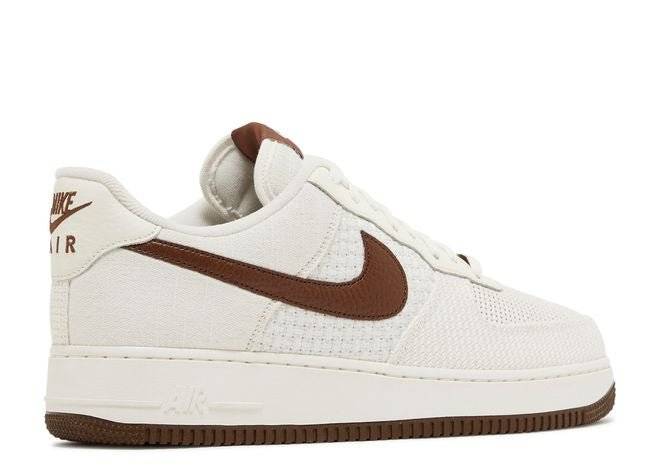 Side view of Nike Air Force 1 07 SNKRS Day sneaker featuring white mesh upper, brown leather Swoosh, and durable cushioning.