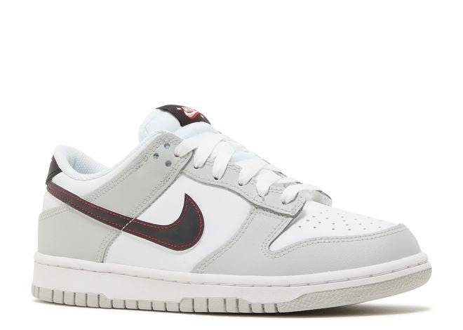 Side view of Nike Dunk Low SE GS Lottery Pack featuring grey fog overlays, black Swoosh with red stitching, and cushioned sole.