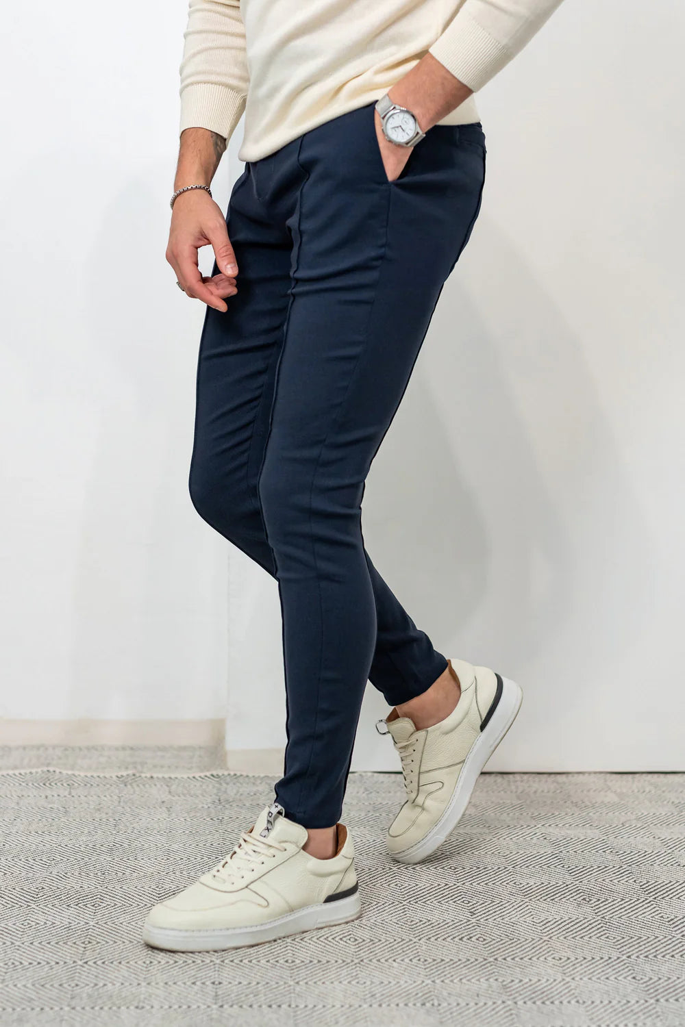 Milan Trousers Navy paired with a cream sweater and beige sneakers, emphasizing a versatile and stylish wardrobe essential.