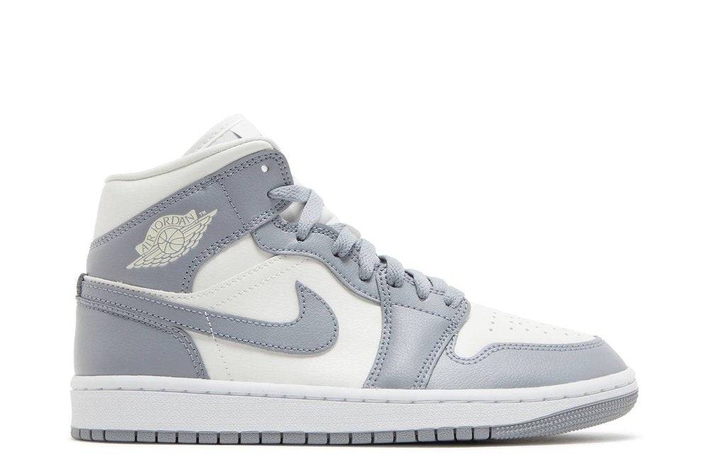 Wmns Air Jordan 1 Mid Stealth sneaker in grey and white leather with a debossed collar wings logo and Nike Swoosh, ideal for casual wear.