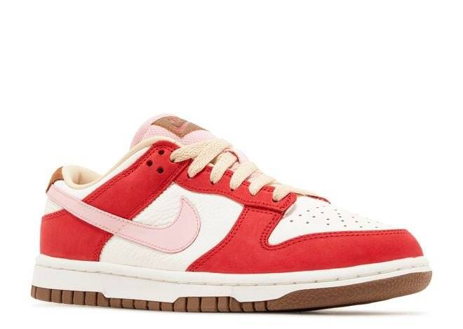 Nike Dunk Low PRM Bacon for women with a Sport Red and white upper, pink Swoosh, and Medium Brown outsole in a side-front angled view.