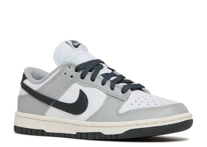 Side angle of Wmns Dunk Low Light Smoke Grey sneaker showcasing white leather base, grey overlays, and black Swoosh with matching laces.